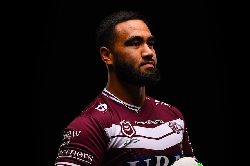 A photo of Keith Titmuss posing in a maroon Manly jersey on a black background.