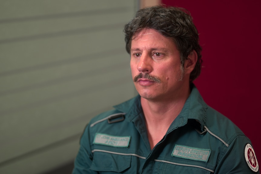 A man in paramedic fatigues looks solemnly into the middle distance.