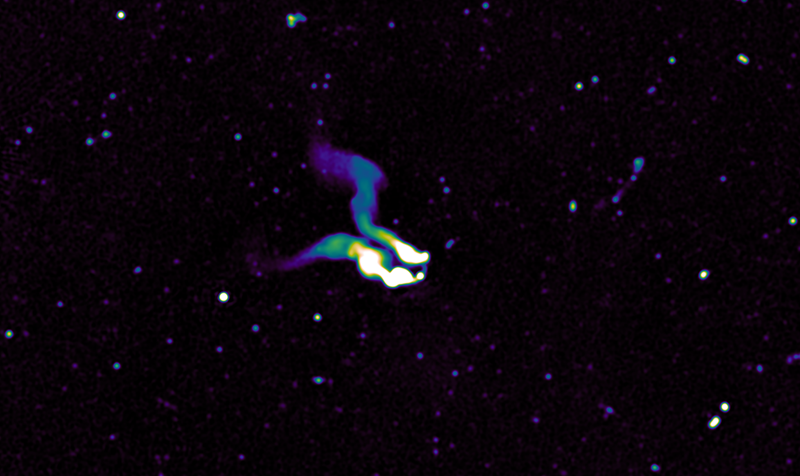 A dark black sky is dotted with spots of light. In the centre of the image one spot has two bright white tails extending out in parallel, fading to blues and purples the further they reach from the central spot. These are jets from a supermassive blackhole.