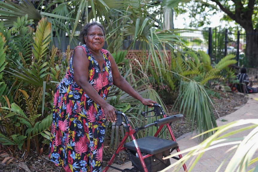 A woman smiles to the camera and holds a walker.