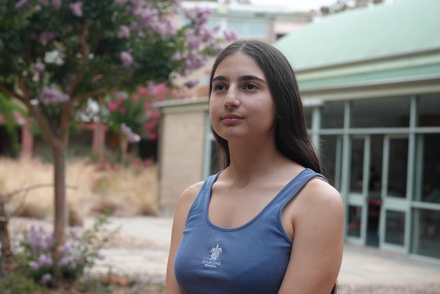 A young woman with dark hair looks beyond camera. Flowering tree in background.