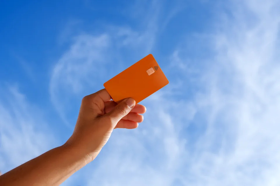 Person holding a credit card against a blue sky, symbolizing financial freedom or digital transactions