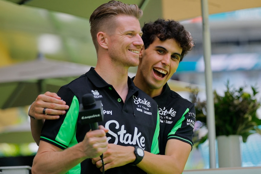 An F1 driver playfully hugs his teammate during a fan-day event