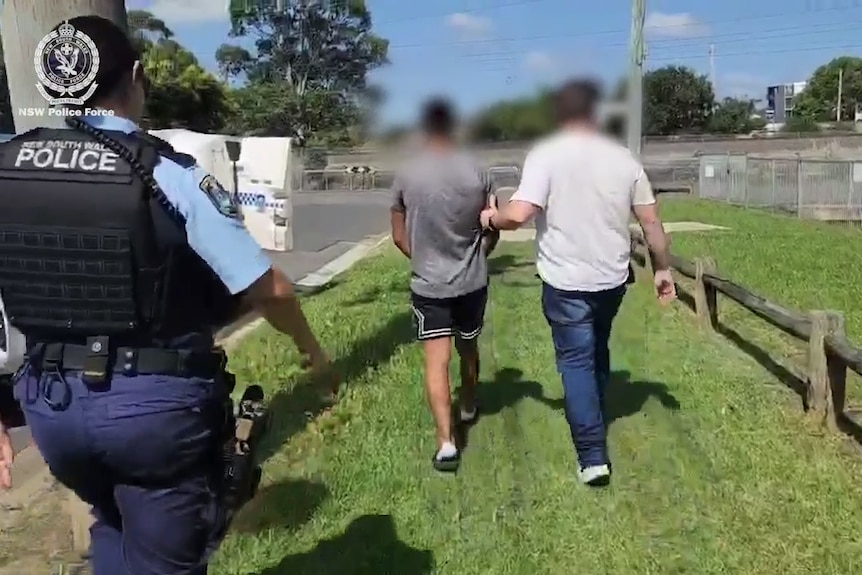 A man with hand cuffs, sitting near grass, his face blurred.