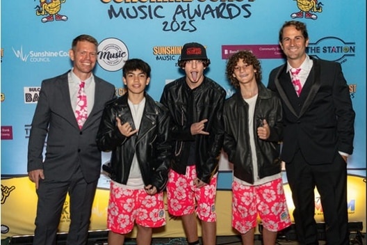 Three teenage boys posing for a photo next to two adult men on a red carpet