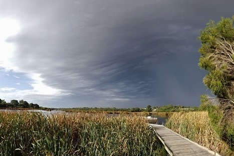 Storm clouds brew over a boardwalk at a lake