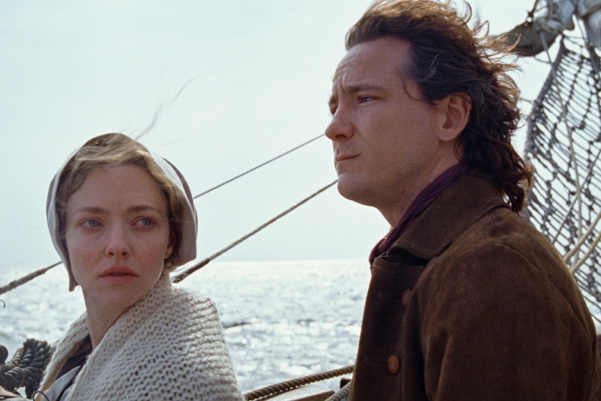 A man and a woman look out to sea on a boat.
