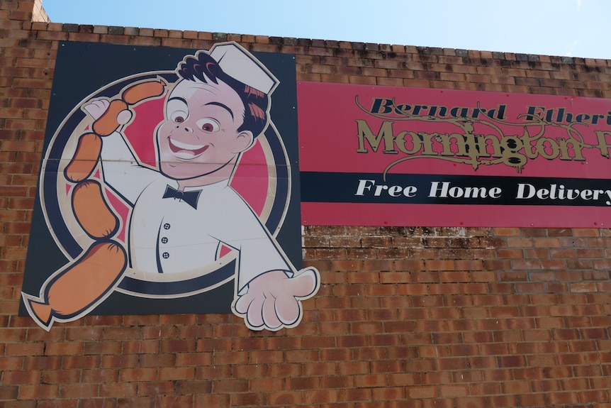 A brick building with a sign of a man holding sausages.