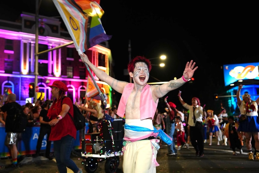 a Mardi Gras participant holds a flag as he smiles and walks down oxford street