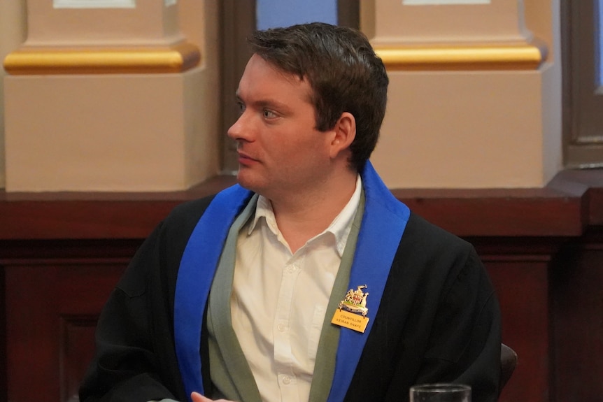 A man with short brown hair wearing a robe