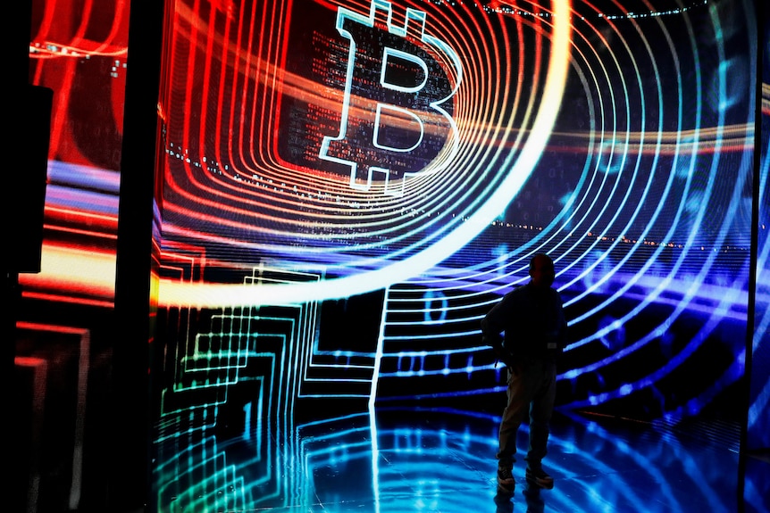 A person's silhouette stands in front of a multicoloured projected graphic of a Bitcoin token.