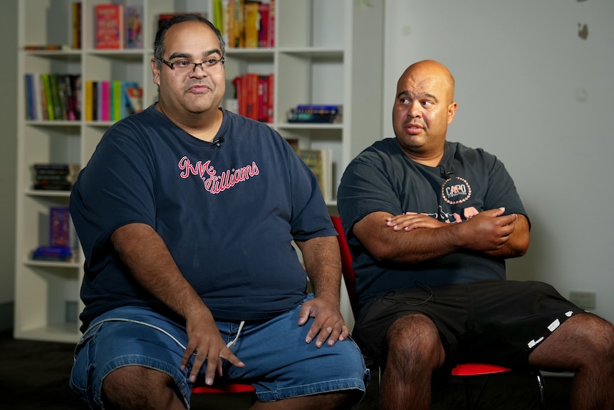 Two men in shorts and T-shirts sitting next to each other.