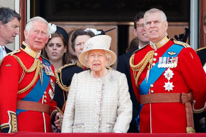 Queen in a hat flanked by Charles and Andrew in red military dress jackets.