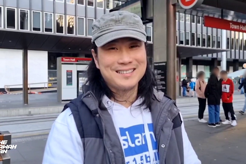 A man in a cap, long-sleeve top and vest smiles for a photo in Sydney's CBD.