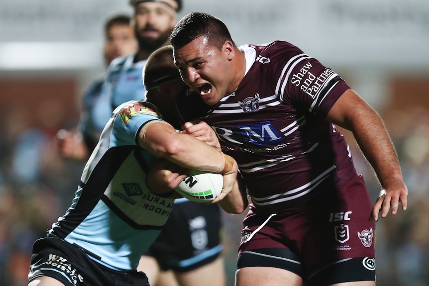Lloyd Perrett of the Sea Eagles is tackled by the Sharks defence
