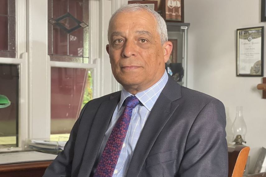 A man wearing a suit and tie sits at a desk.