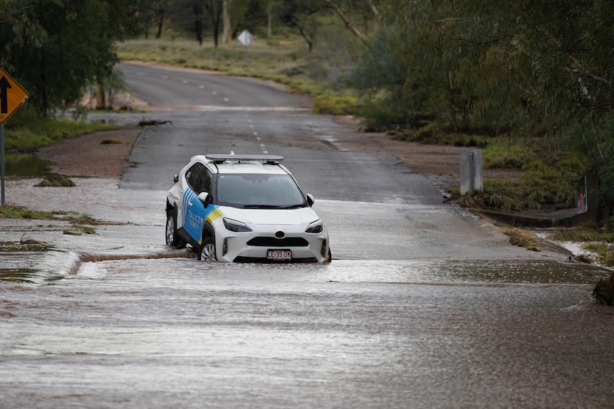 A blue and white security car left on a road covered in floodwaters.