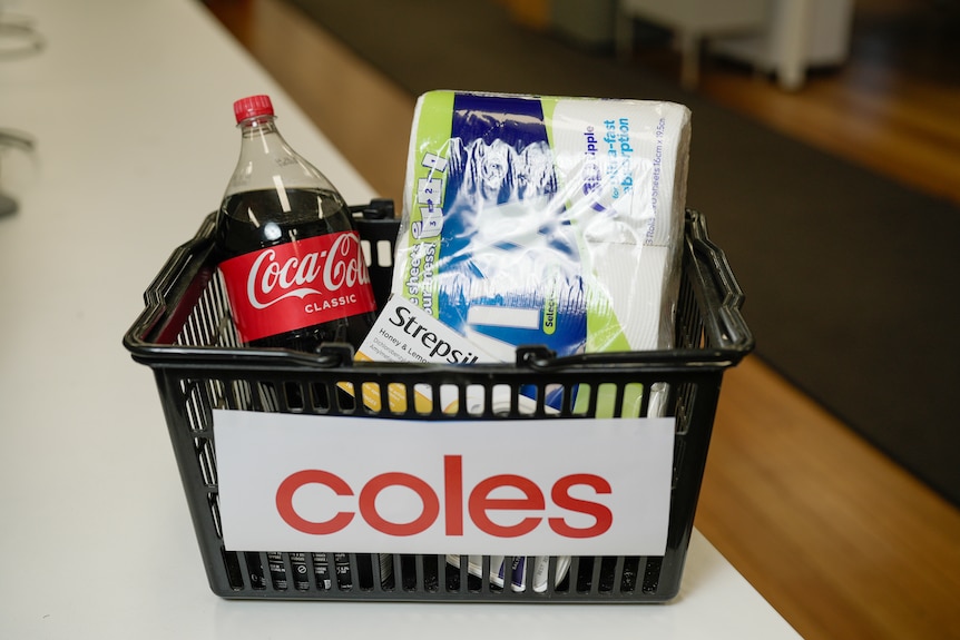A Coles basket filled with groceries including Coca Cola, paper towels and Strepsils.