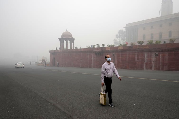 a man in a face msk walks down a street with thick smog