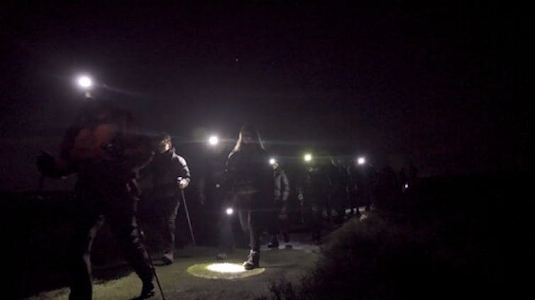 People in the dark walking with head torches during a dark sky event.