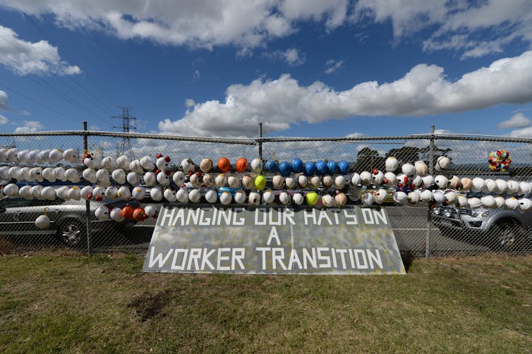 A line of worker helmets hands on a fence outside the Hazelwood power station after it is closed.