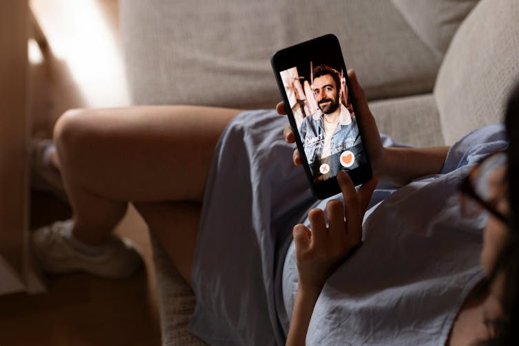 A woman sitting on a couch swiping through a dating app.