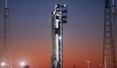 Backdropped by the sunrise, a white and black rocket stands poised on its launch pad