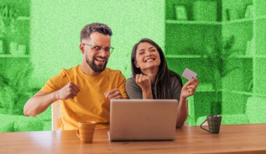 Young couple looking happy, sitting at a table in front of a laptop.