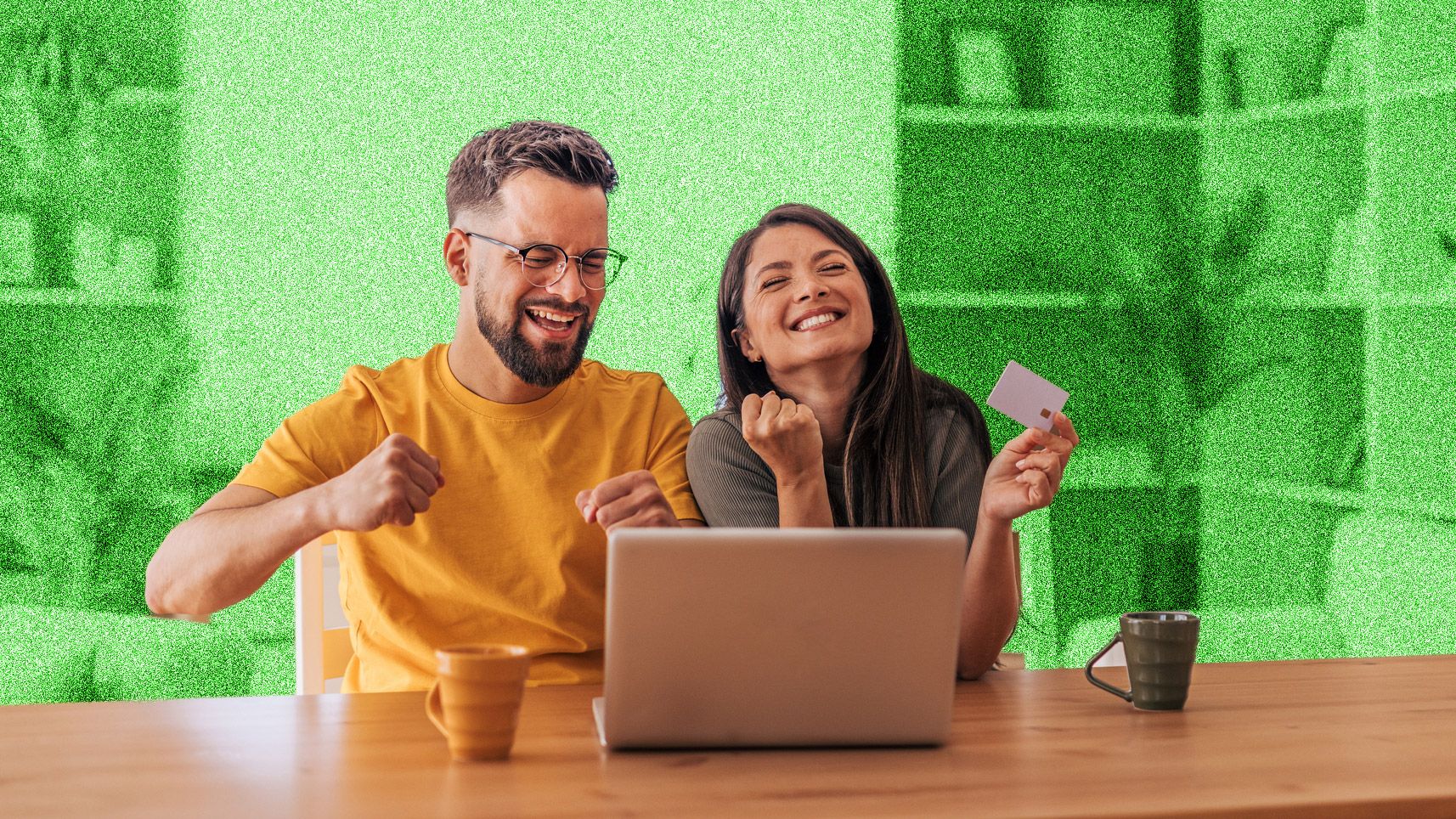 Young couple looking happy, sitting at a table in front of a laptop.
