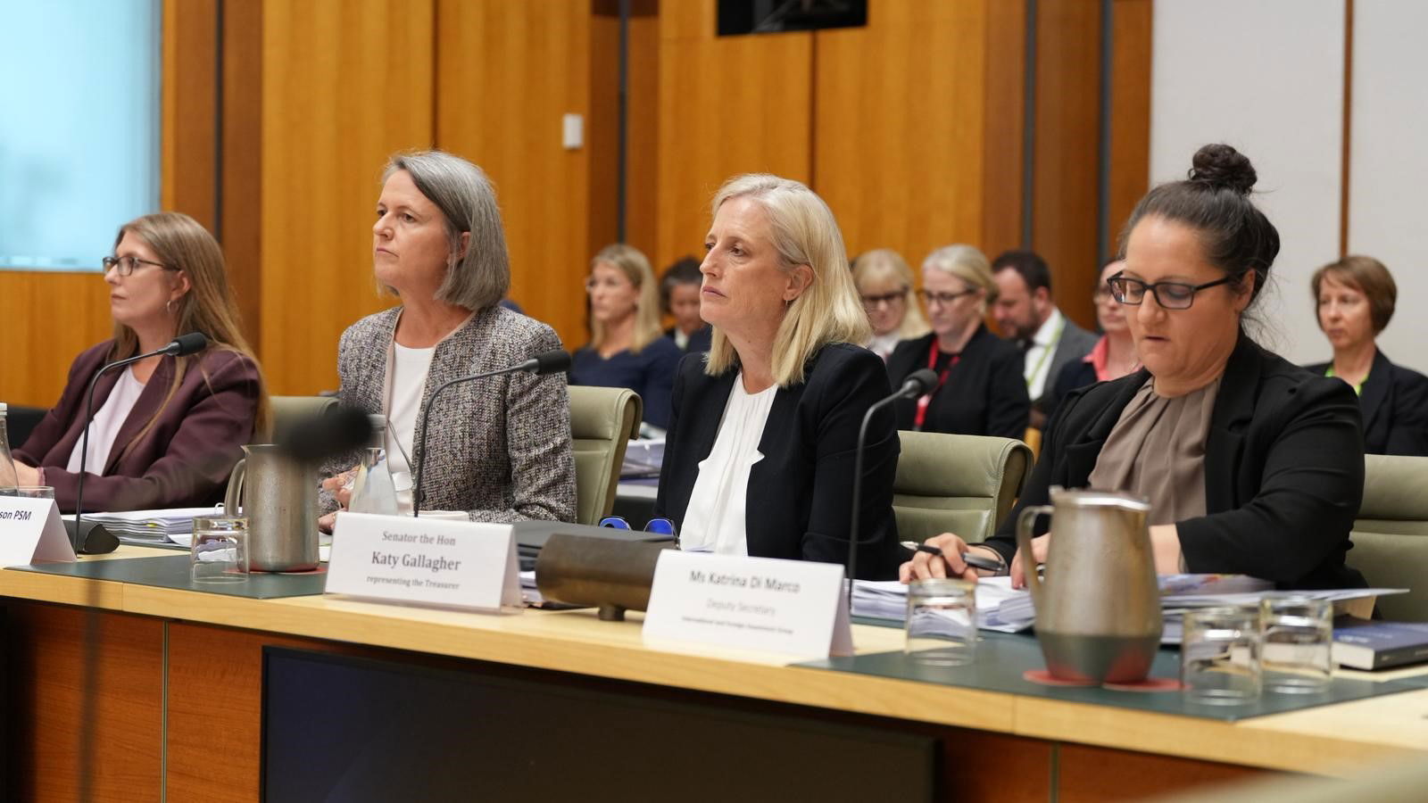 Four women looking serious sit at a desk.