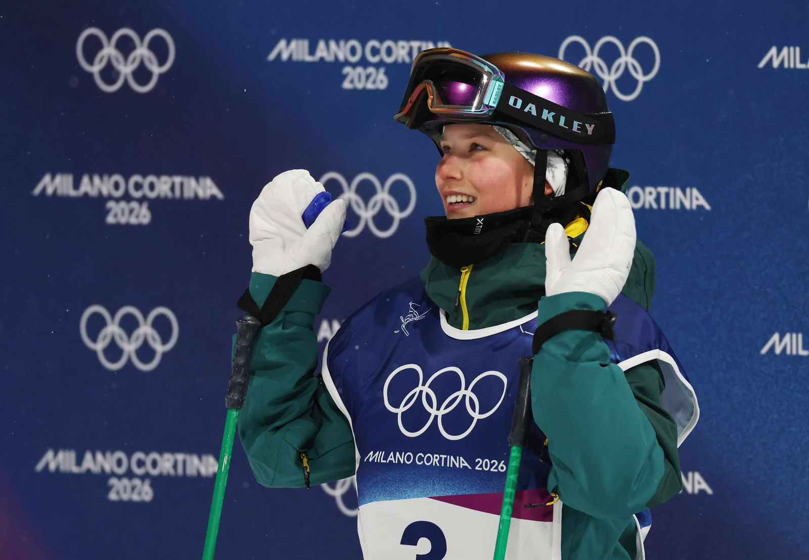 A skier waves at the camera with two hands, wearing helmet and white gloves