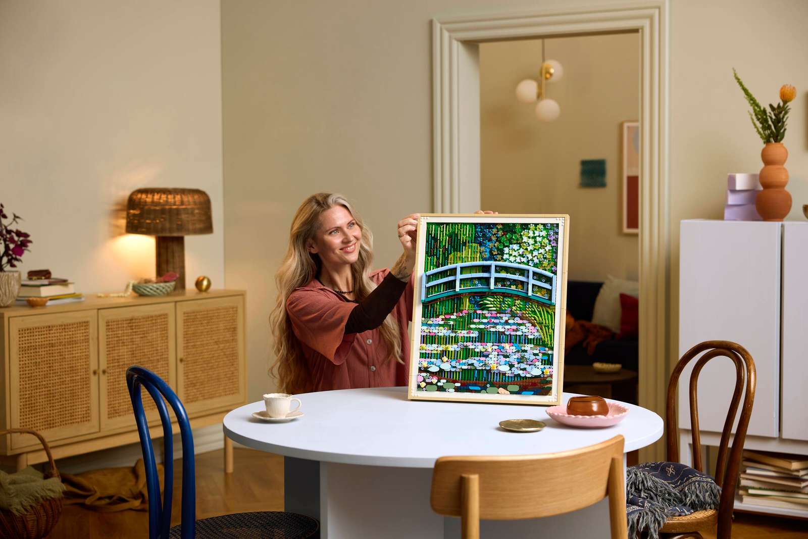 Woman sitting at a table holding up the ‘Monet Bridge Over a Pond of Water Lilies’ LEGO set
