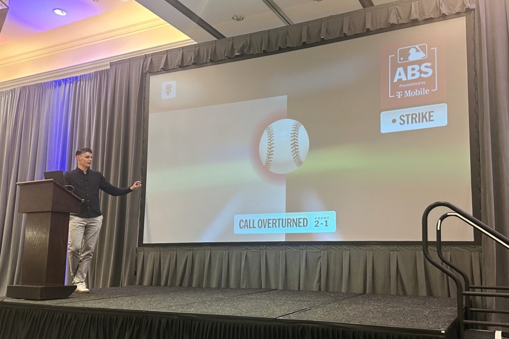 Joe Martinez presenting the new Automated Ball/Strike system with a screen showing a baseball and "CALL OVERTURNED"