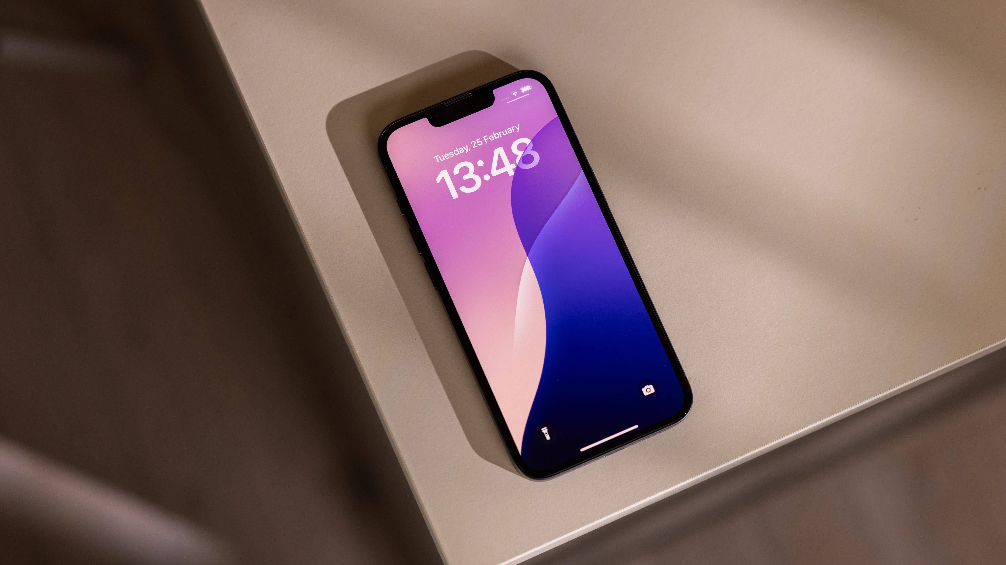 An Apple iPhone 16e lying on a table, displaying the time 13:48 and date February 26.