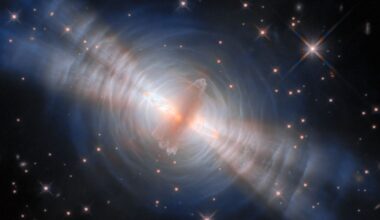 An image of the egg nebula, with a glowing streak of pink gas in the middle surrounded by concentric circles of white like with four diagonal beams of light streaking from top left to bottom right all in front of a deep space starry background