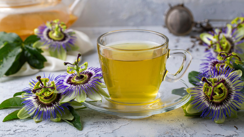 A cup of passionflower tea surrounded by passionflowers on a white background