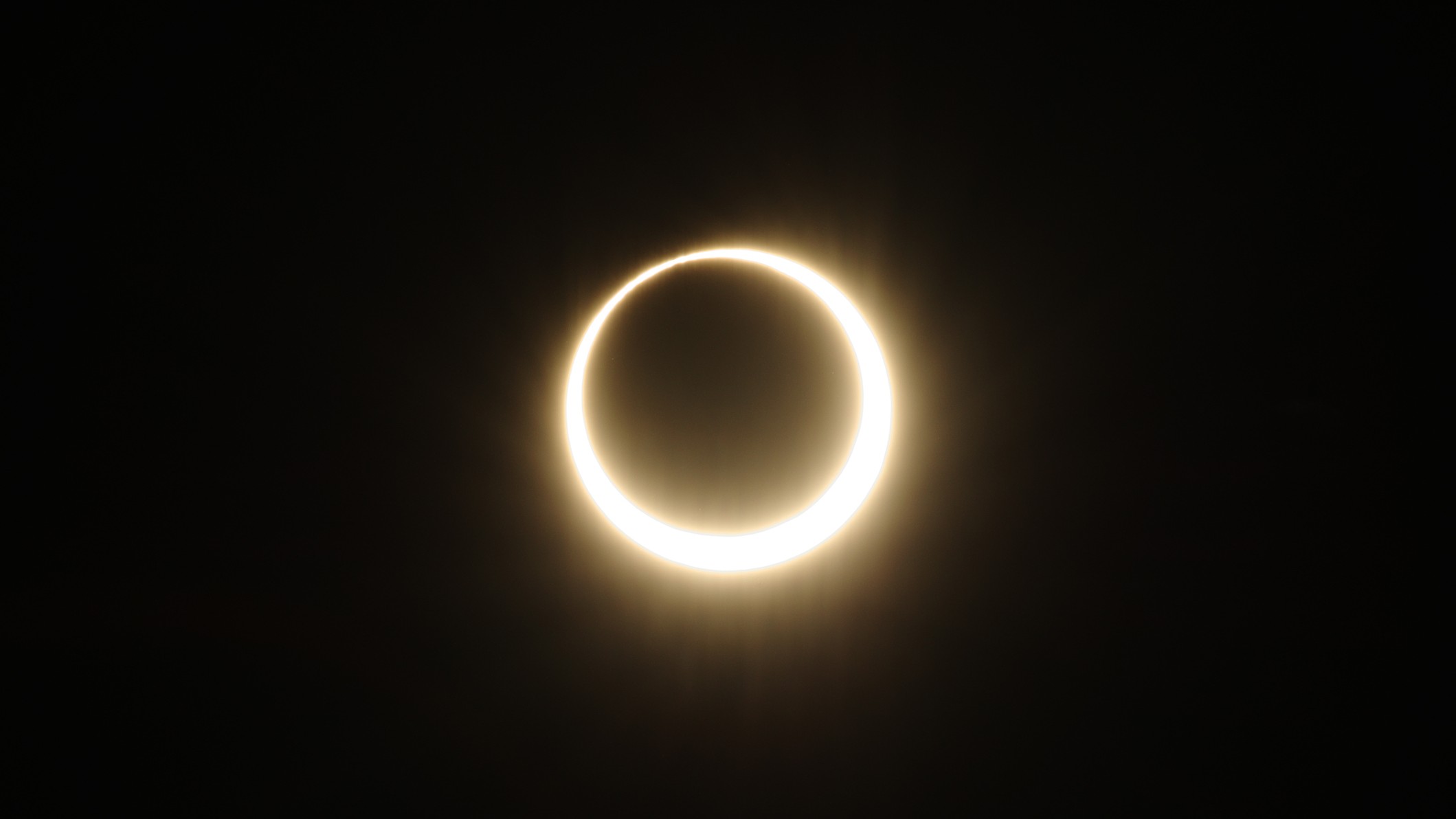 a bright yellow while ring around a black circle against a black background.