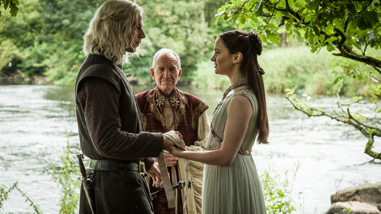 Wilf Scolding as Rhaegar Targaryen and Aisling Franciosi as Lyanna Stark holding hands during a wedding in Game of Thrones