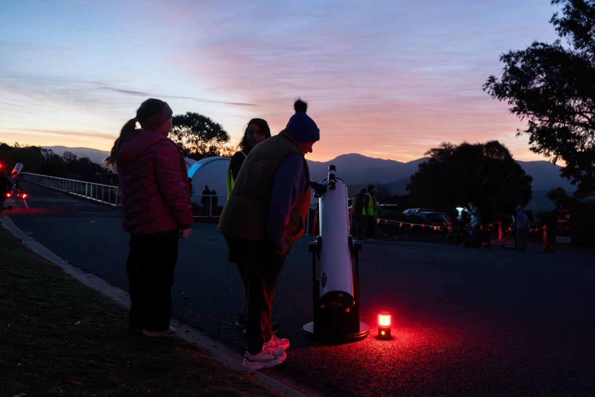 A group of people huddled around a telescope at sunset. 