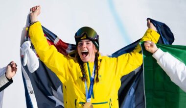 An athlete celebrates with a gold medal around her neck and an Australian flag draped behind her with her arms raised.