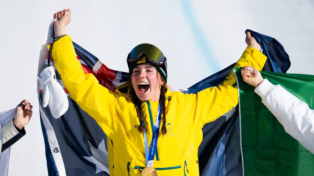 An athlete celebrates with a gold medal around her neck and an Australian flag draped behind her with her arms raised.