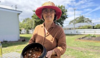 Woman in an orange hat and orange shirt smiles and holds a black pot full of kimchi