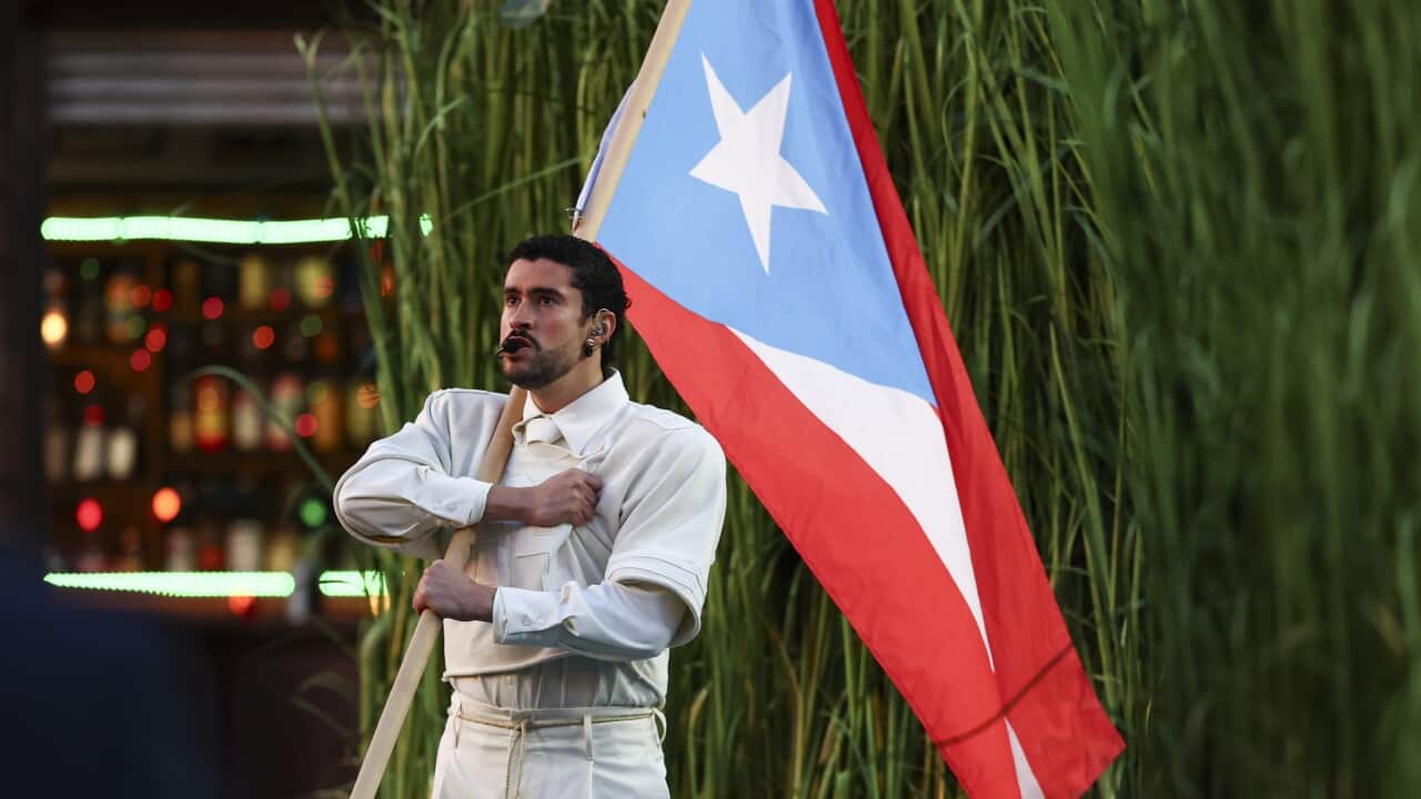 A man holding a Puerto Rican flag in front of long grass.