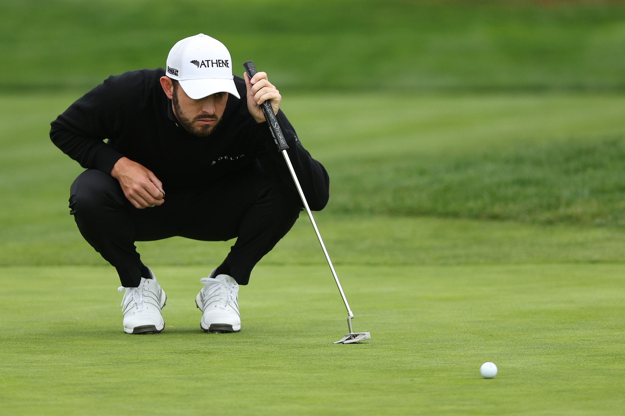 Patrick Cantlay lining up a putt on the green while resting on his putter in a crouched position