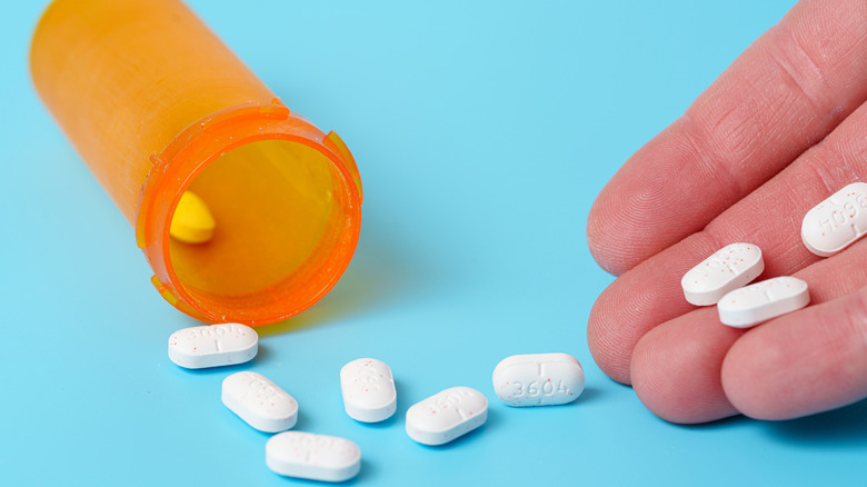 Pills spilling out of a plain orange bottle with a hand holding several