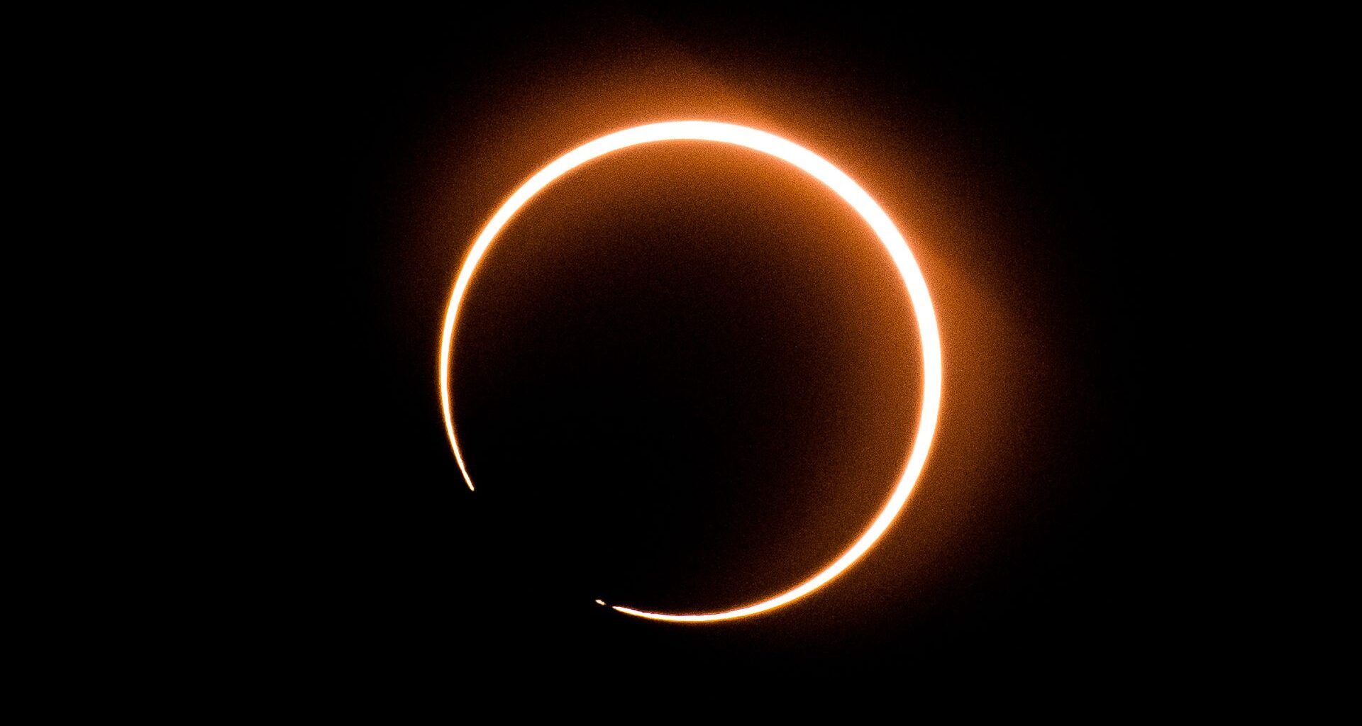 The outline of the sun is visible surrounding the moon during a solar eclipse, with a small break in the circle to the lower left.