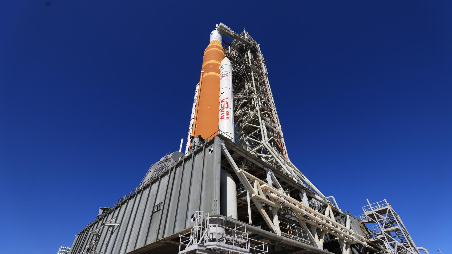 a tall white and orange rocket upright on a launch pad under a blue sky