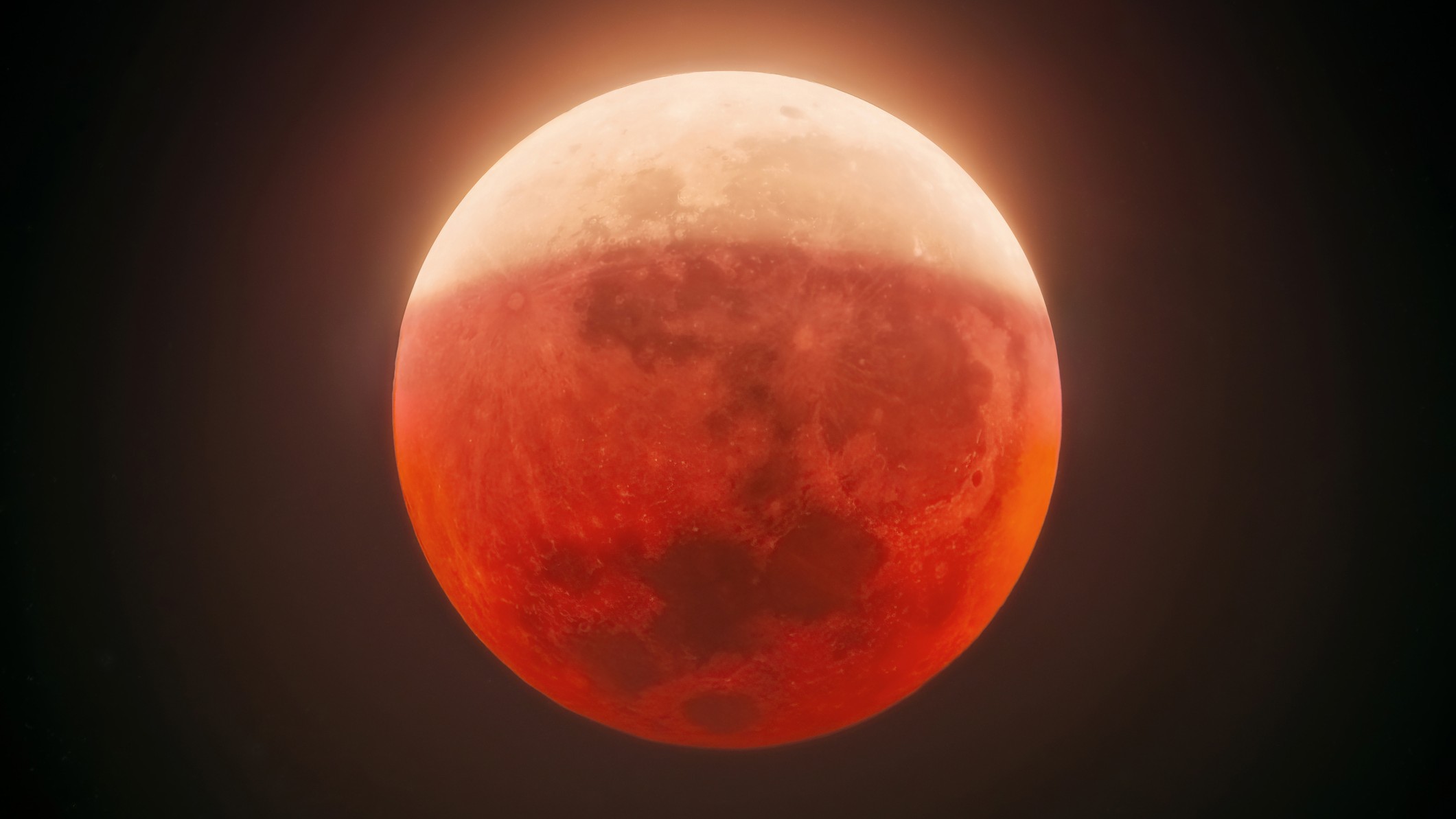 close up view of partial lunar eclipse with the lower portion of the moon colored crimson red and the upper portion a lighter brighter white hue.