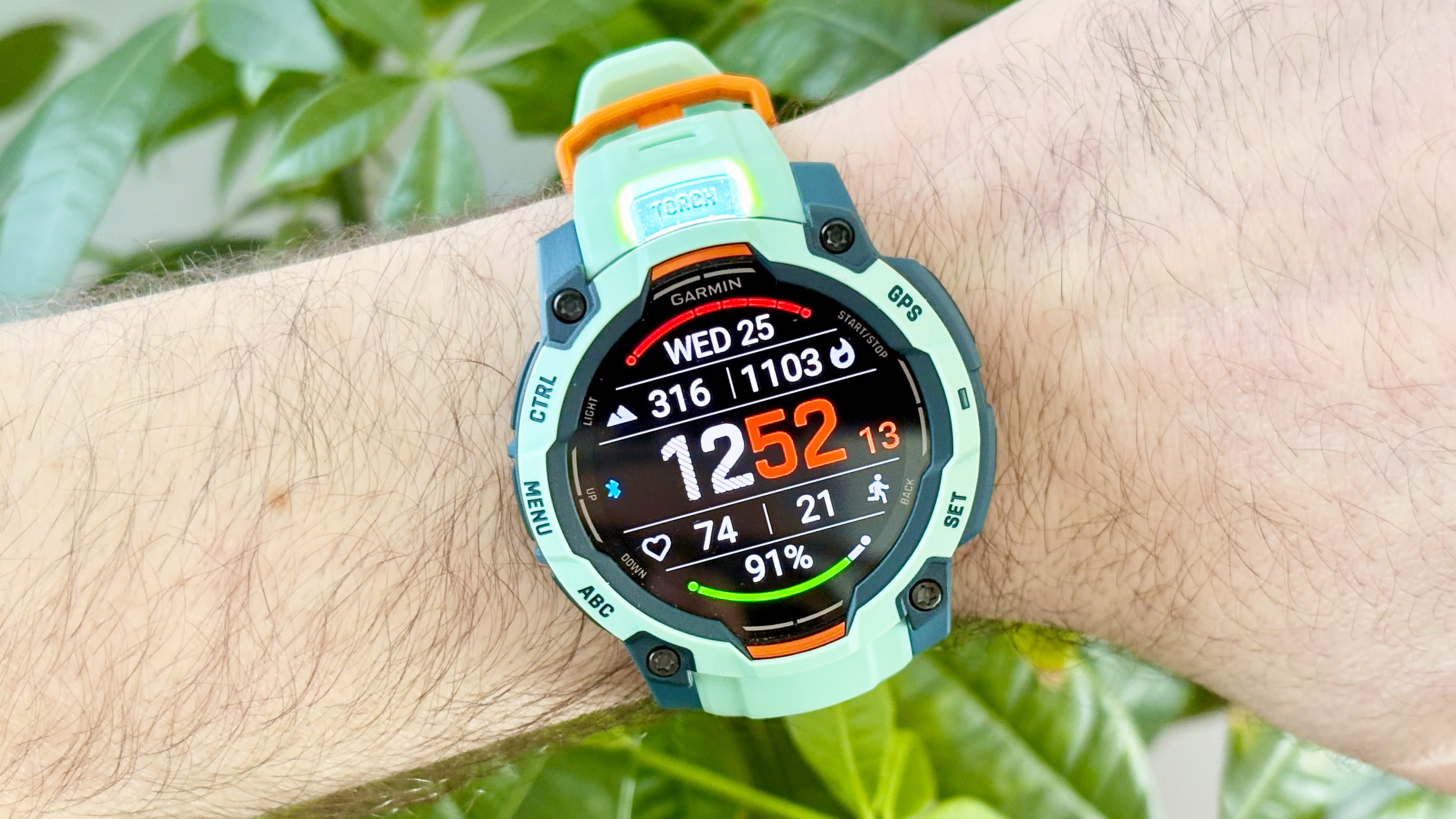 Close-up of the Garmin Instinct 3 showing the 'Torch' LED flashlight illuminated from the top of the watch case