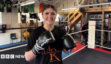 Megan Redstall raises her boxing gloves for the camera as she stands in the ring.